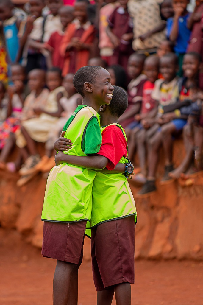 Two young participants smiling and sharing a warm hug in sports bibs on the pitch